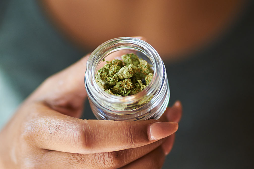 african american woman opening bottle of legal marijuana from dispensary close up with selective focus on weed